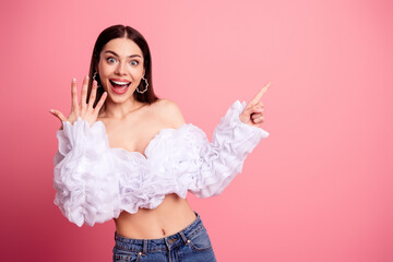 Excited young woman showing off ring and pointing enthusiastically against a pink background...