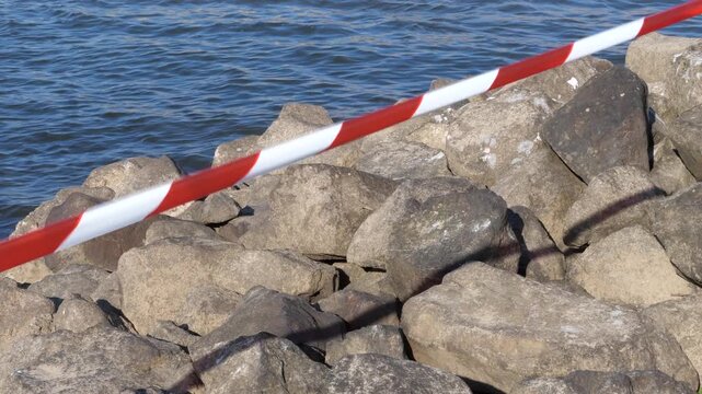 Red and white warning tape over a rocky riverbank close-up shot