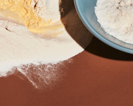 White flour and icing sugar drifts on a dark cocoa brown surface, featuring a powdery tactile texture for food packaging and background design