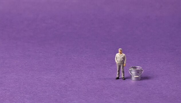 Saturated purple surface with a tiny person in work clothes standing beside a small paint bucket, a minimal conceptual scene for creative advertising and copy space