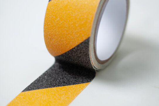 Roll of black and yellow anti-slip safety tape with diagonal hazard stripes on a white background. Ideal for floor traction, stair safety, industrial marking and slip prevention in workspaces