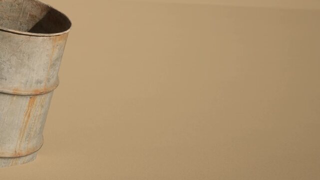 A metal bucket sits on a brown surface. The bucket is made of metal and reflects light. There are no other objects in the scene. This setting is minimal and focuses on the bucket.