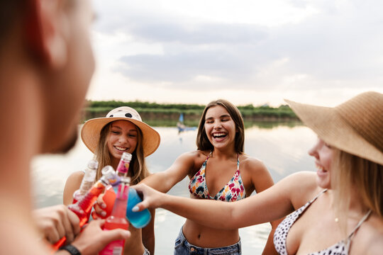 Friends Gather by the River in Summer Enjoying Drinks and Having Fun Together