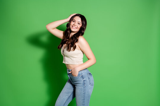 Smiling young woman in jeans and crop top posing against a green background, casual fashion portrait conveying confidence, happiness and relaxed modern style