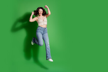 Happy young woman jumping in studio against green background, casual outfit celebrating joy and...