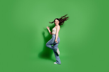 Young woman jumping and smiling with energetic pose on a green background in casual jeans and tank...
