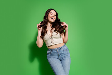 Happy young woman smiling in casual jeans and lace-up crop top against a bright green background...
