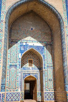Magnificent historic Islamic architecture in Bukhara, Uzbekistan, featuring a monumental pointed arch decorated with intricate blue and turquoise tilework, geometric mosaics, brick patterns