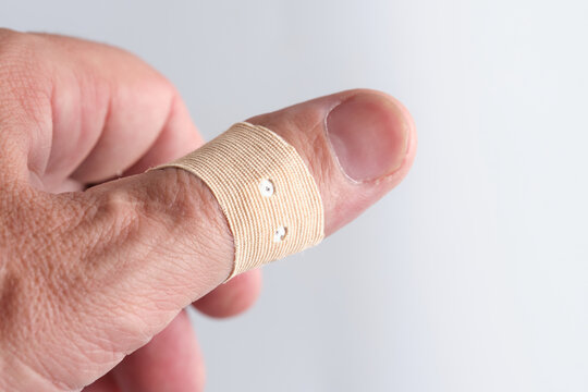 Male thumb wrapped with fabric adhesive bandage plaster for first aid care and minor injury protection.