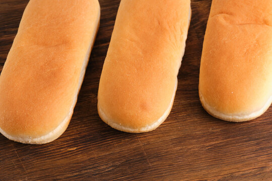 Close up view three freshly baked soft hot dog buns lying on rustic dark wooden table background.