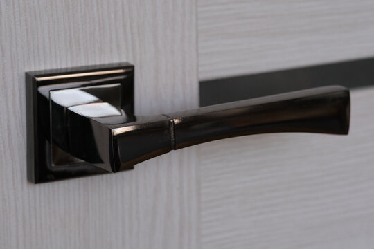 Modern shiny dark metallic door handle mounted on light wooden panel close up shot.