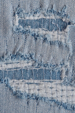Vertical close up view light blue ripped jeans material with layered white horizontal frayed threads.