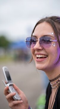 Laughing woman wearing purple sunglasses and holding flip phone outdoors with joy and confidence