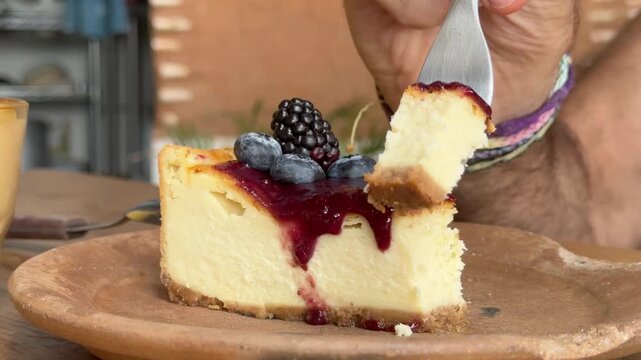 Fork Taking Bite of Baked Cheesecake topped with Berry Compote and Fresh Berries