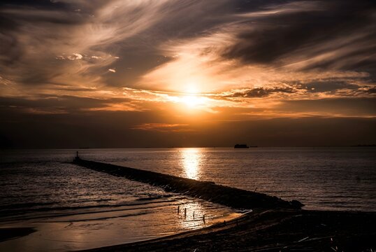 A brilliant golden sun breaks through layered clouds above the sea, casting a long luminous reflection across the water and creating a dramatic, richly textured coastal sunset.