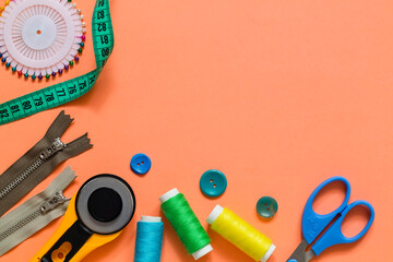 Tailoring and sewing accessories arranged on a coral background with thread spools, scissors,...
