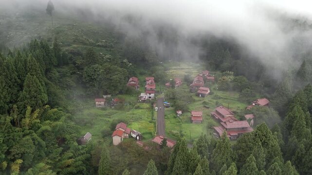 Aerial view of Ozuchi, a historic preservation district with traditional houses nestled among lush green forests and misty hills in Kaga, Ishikawa, Japan.