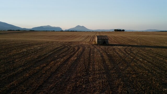 Aerial view of a stone hut at the edge of a harvested field with distant mountains at sunrise, Valensole plateau, Provence, France