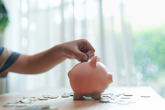 Child puts a coin into a piggy bank surrounded by savings at home, representing money saving, financial education, budgeting, responsibility, savings goals