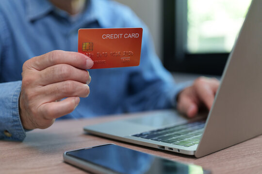 Man holding a credit card while using a laptop at home, representing online shopping, digital payment, e-commerce, internet banking, secure checkout, consumer spending and cashless purchasing.