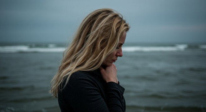 Sad blonde woman standing alone by the stormy sea, expressing anxiety, loneliness and emotional distress