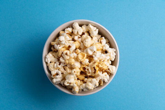 Fresh organic popcorn in an orange bowl on a blue background