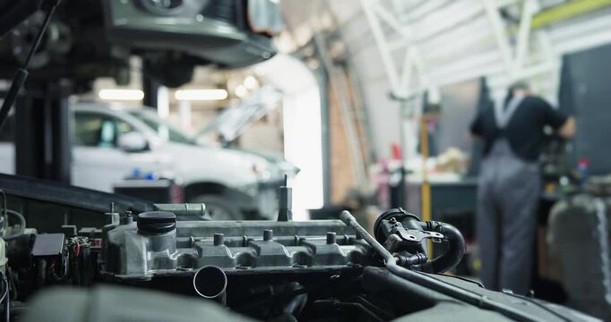Mechanic servicing car engine in auto repair garage with shallow focus and blurred background.
