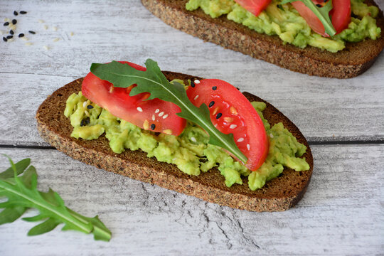 Avocado and Tomato Toast with smashed avocado and arugula on Wooden Table, close up