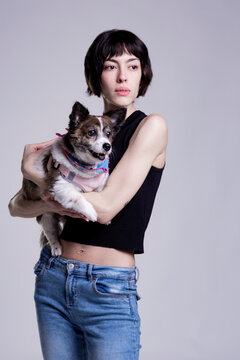 Stylish Model in Blue Jeans Sitting on Steel Chair in Minimalist Studio Setting with her dog