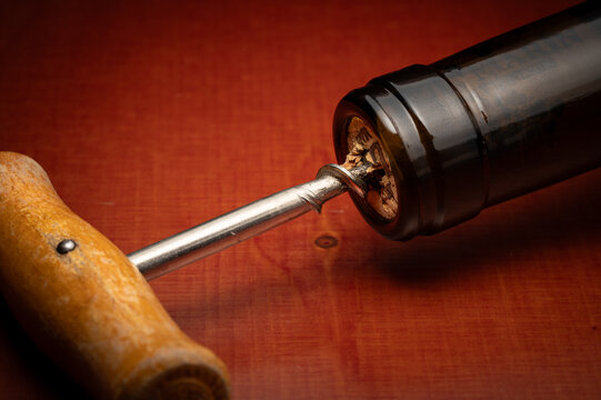 Corkscrew in a cork af a bottle of wine on a red wooden plate