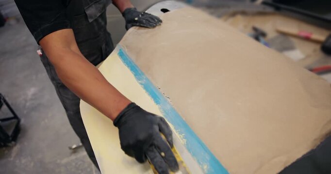 Tracking shot worker smoothing body filler on car panel door in auto workshop overhead handheld closeup.