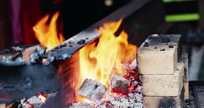 Metal bar heating over open forge fire on brick hearth in workshop of blacksmith.