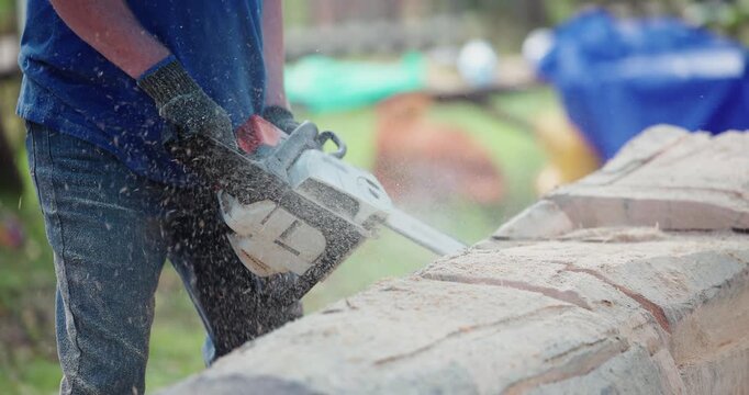 Worker cutting large tree log with chainsaw on outdoor worksite.