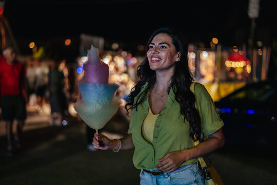 Woman enjoying colorful cotton candy at night fair
