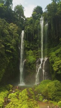 Aerial view of the lush Sekumpul Waterfall surrounded by dense tropical rainforest and greenery in Kecamatan Sawan, Bali, Indonesia.