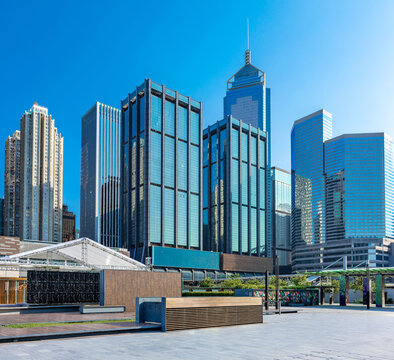 Contemporary high-rise architecture framing an open urban plaza in Wan Chai, Hong Kong, with reflective glass facades beneath an expansive blue sky.
