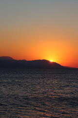 Fototapeta premium Beautiful orange sunset over the Corinthian Gulf in Loutraki, Greece, with the sun setting behind the distant Geraneia Mountains, creating a romantic and colorful Mediterranean seascape. 