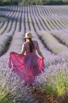 Woman in pink dress walks through lavender field under sunny sky