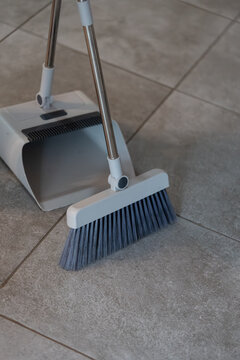 Floor cleaning setup with a brush and dustpan on tiled floor. The broom and dustpan are designed for easy cleanup of dust and dirt, enhancing home cleanliness and convenience.