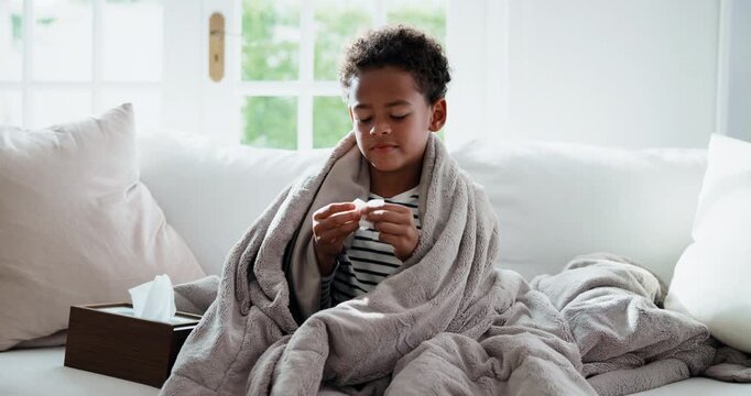 Sick, child and blowing nose with tissue in home for influenza, viral infection or illness. Kid, boy or cold with flu, toilet paper or blanket on sofa for virus, hayfever or bad allergies in house