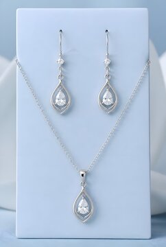 Delicate Silver Teardrop Earrings and Pendant Necklace Jewelry Set With Crystal Accents on Light Blue Display