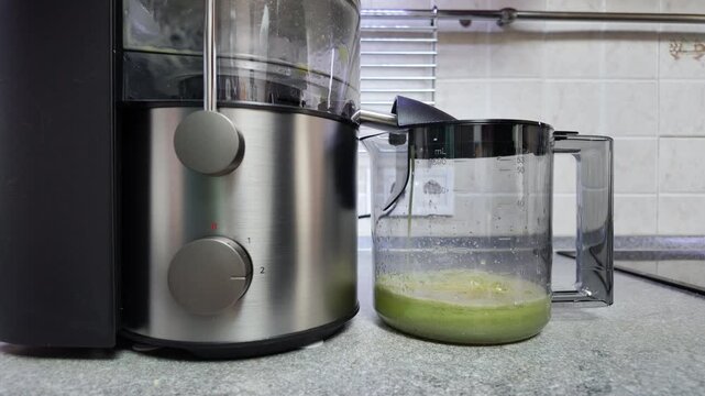 Electric juicer extracting fresh green juice filling transparent pitcher in kitchen for healthy lifestyle, time-lapse