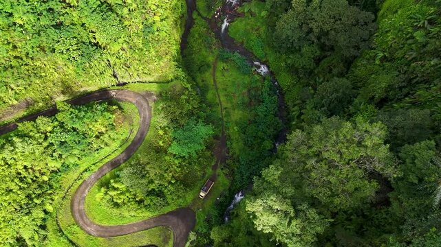 Aerial view of a winding road through lush tropical forest near Curug Ciarjuna in Garut, West Java, Indonesia.