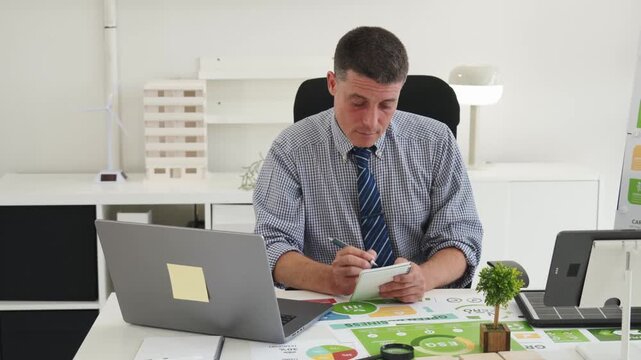 Focused Businessman Reviews Financial Document at Modern Office Desk with Laptop and Reports