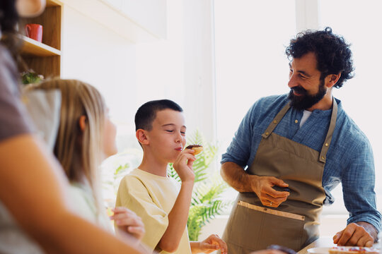 Father watching son enjoy homemade food during family baking at home
