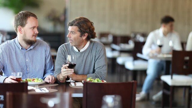 Meeting of two friends in a modern restaurant - two men drinking wine and sharing news. High quality 4k footage