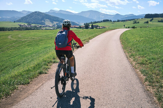 Attractive senior woman riding an electric bicycle on a mountain biking tour through sunny alpine meadows and scenic mountain landscapes above Balderschwang, Allg&auml;u Alps, Bavaria, Germany.