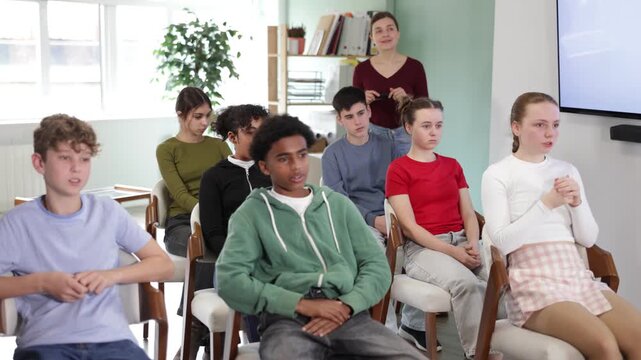 Focused group of diverse teens attending educational session with instructor speaking in school classroom