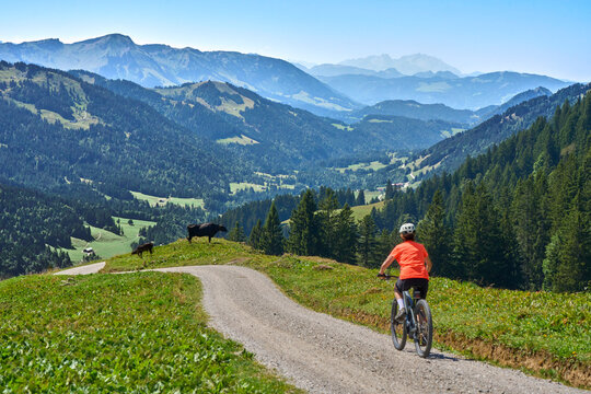 Attractive senior woman riding an electric bicycle on a mountain biking tour through sunny alpine meadows and scenic mountain landscapes above Balderschwang, Allg&auml;u Alps, Bavaria, Germany.