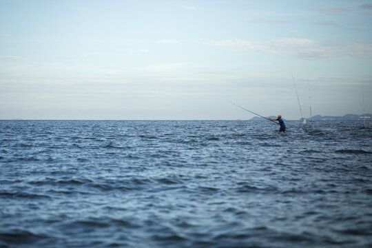 Fisherman standing in water fishing with rod in open tropical sea with blue sky and copy space, Thailand